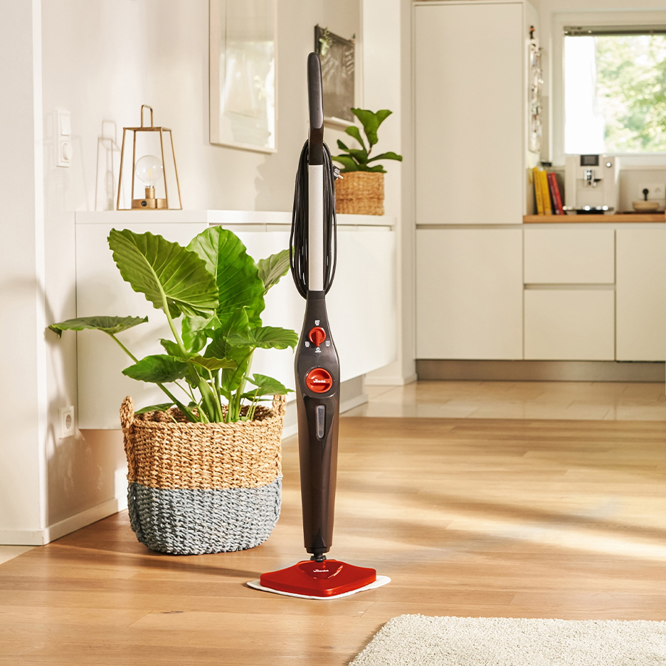 Parni čistač na drvenom podu u modernoj kuhinji sa biljkama.