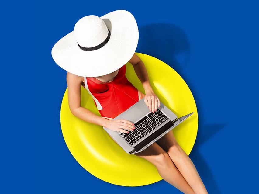 Žena u crvenom kupaćem kostimu i belom šeširu radi na laptopu dok sedi na žutom gumenjaku.