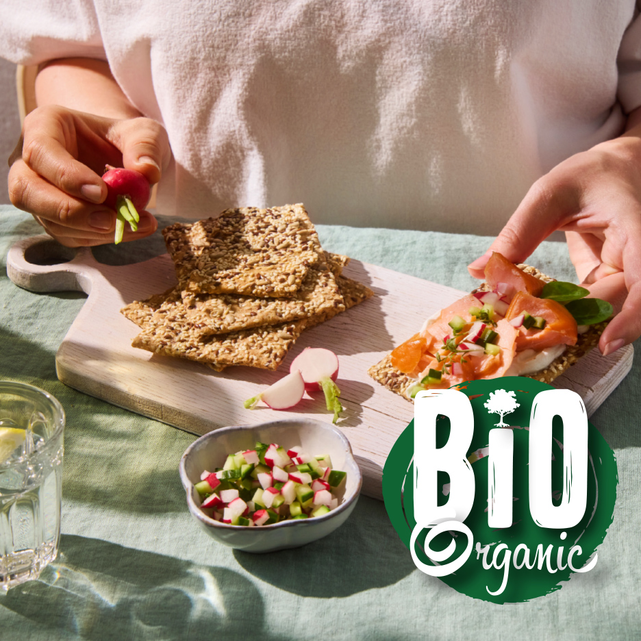 Žena priprema krekere sa lososom i povrćem, sa natpisom „BIO Organic“.