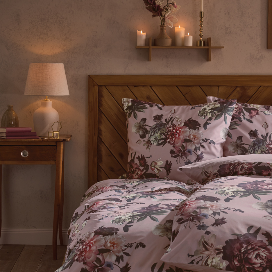 Spavaća soba sa cvetnom posteljinom, noćnim stočićem sa lampom i policom sa svećama.