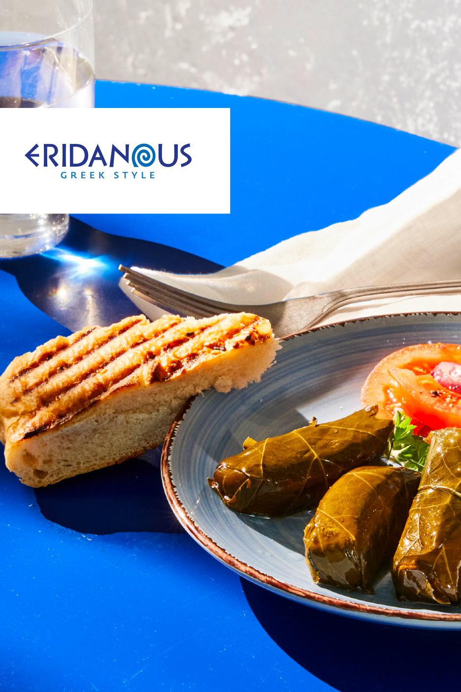 Grilovana lepinja, sarmice od vinove loze i paradajz na plavom stolu.