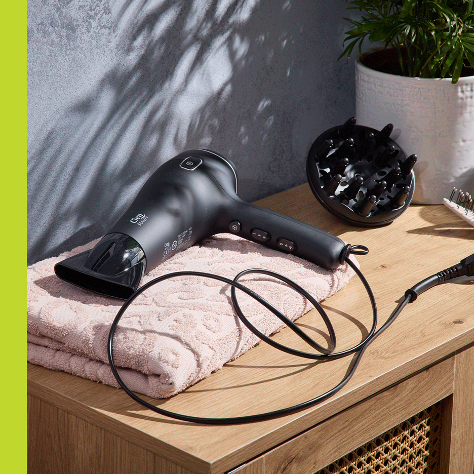 Crni fen za kosu sa difuzorom i peškirom na drvenom stolu.