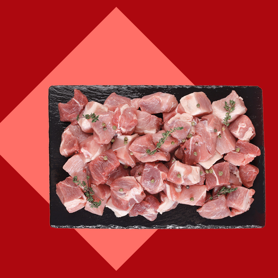 Sveže isečeno svinjsko meso na crnoj ploči, ukrašeno začinskim biljem i biberom.