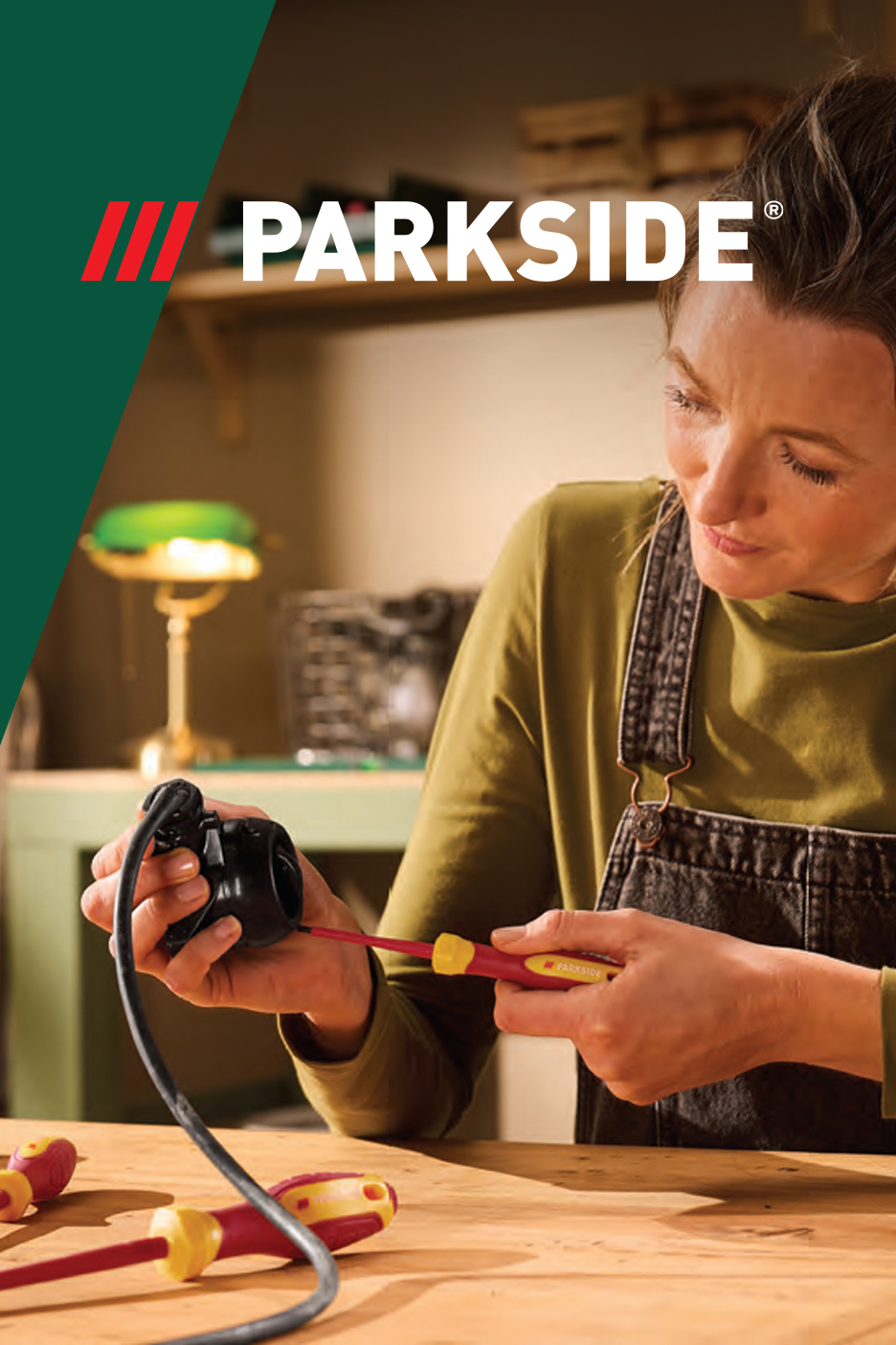 Žena popravlja električni uređaj šrafcigerom, sa drugim šrafcigerima na stolu.