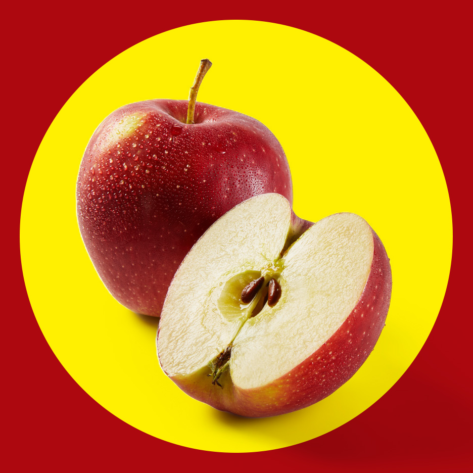 Crvena jabuka sa kapljicama vode i prepolovljena jabuka sa semenjem na žutoj pozadini