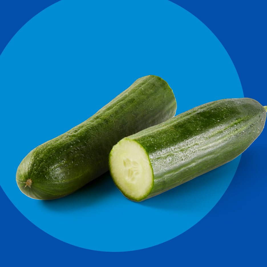 Dva sveža krastavca, jedan ceo i jedan prepolovljen, na plavoj pozadini.