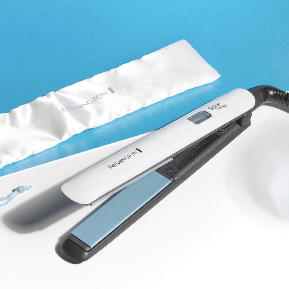 Bela pegla za kosu sa plavim pločama i belom torbicom na plavoj i beloj pozadini.