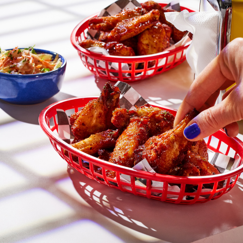 Dve korpe sa pilećim krilcima i činija salate od kupusa, ruka uzima krilce.