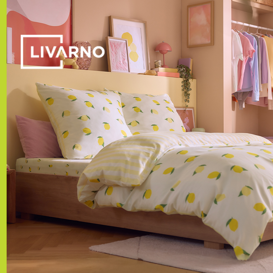 Spavaća soba sa posteljinom sa dezenom limuna, ružičastim jastukom i otvorenim ormarom.