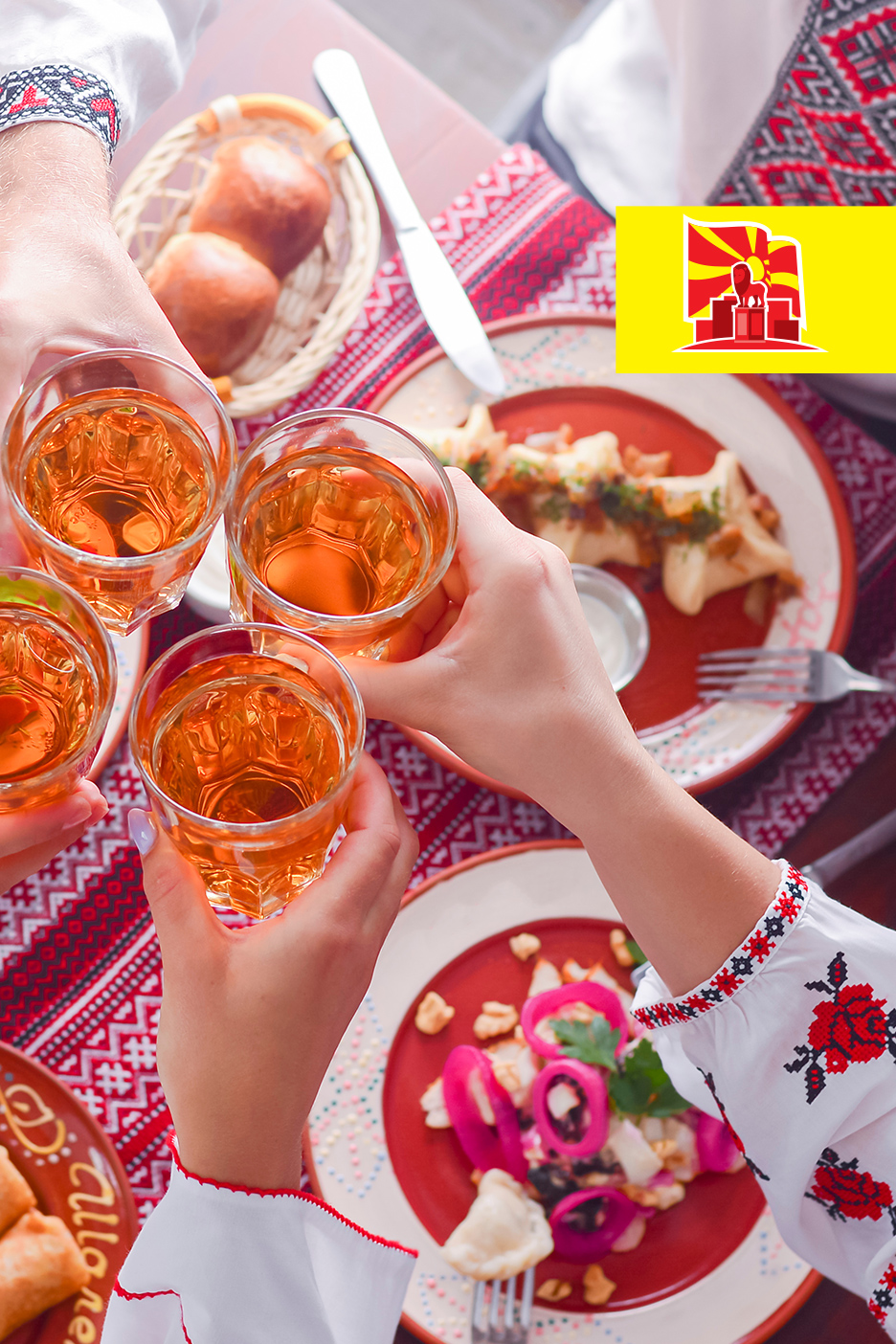 Ljudi nazdravljaju pićem za stolom sa tradicionalnom hranom i vezenim rukavima.