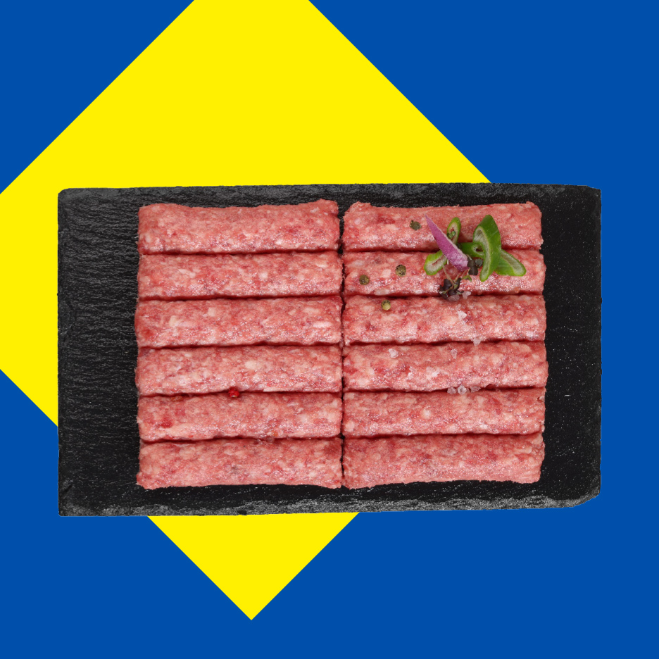 Sveži ćevapi na crnoj ploči, ukrašeni začinima, na žuto-plavoj pozadini.