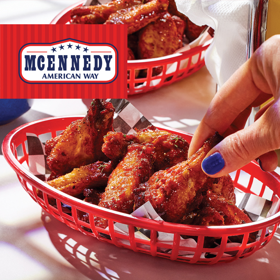 Prženi pileći bataci u crvenoj korpi sa kariranim papirom, ruka uzima jedan.